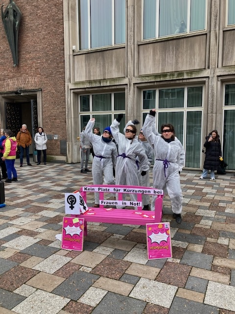 Der Verein FrauenLeben bei einer Protestaktion - im Vordergrund eine pinke Bank: " Kein Platz für Kürzugen bei Frauen in Not." steht darauf.