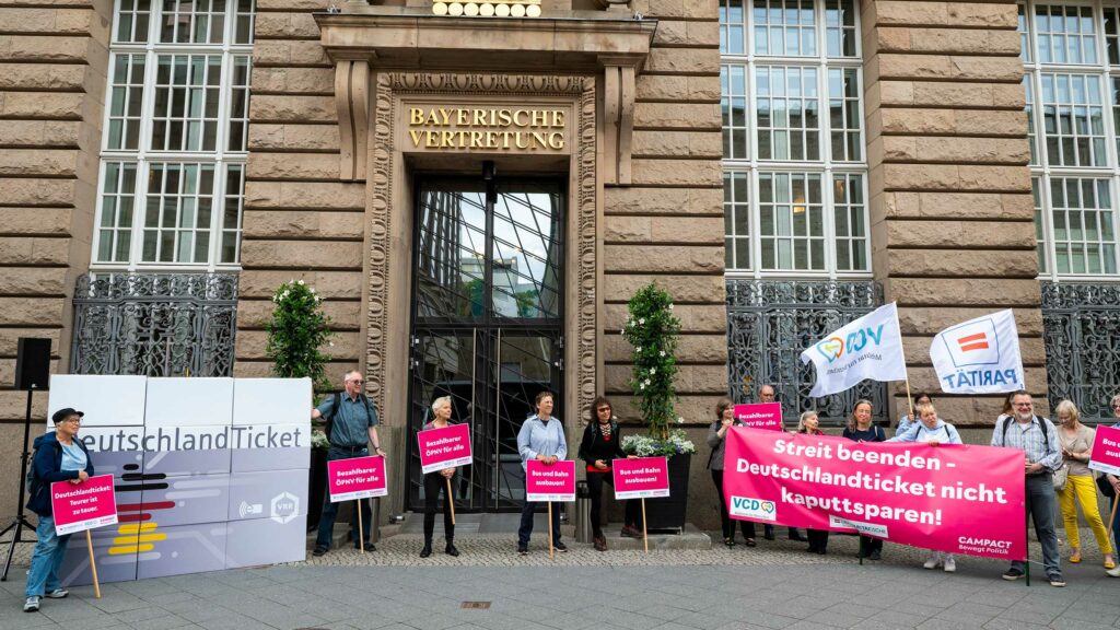 Protest vor der Verkehrsministerkonferenz. Auf einem großen Banner steht: "Streit beenden – Deutschlandticket nicht kaputtsparen!"