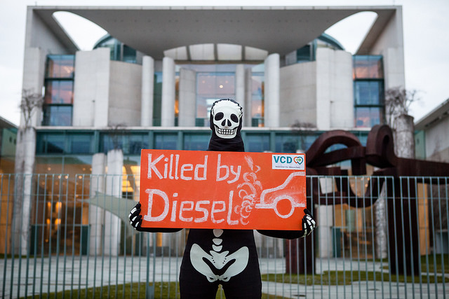 Skelett steht vor dem Bundeskanzleramt und protestiert mit Schild "Killed by Diesel"