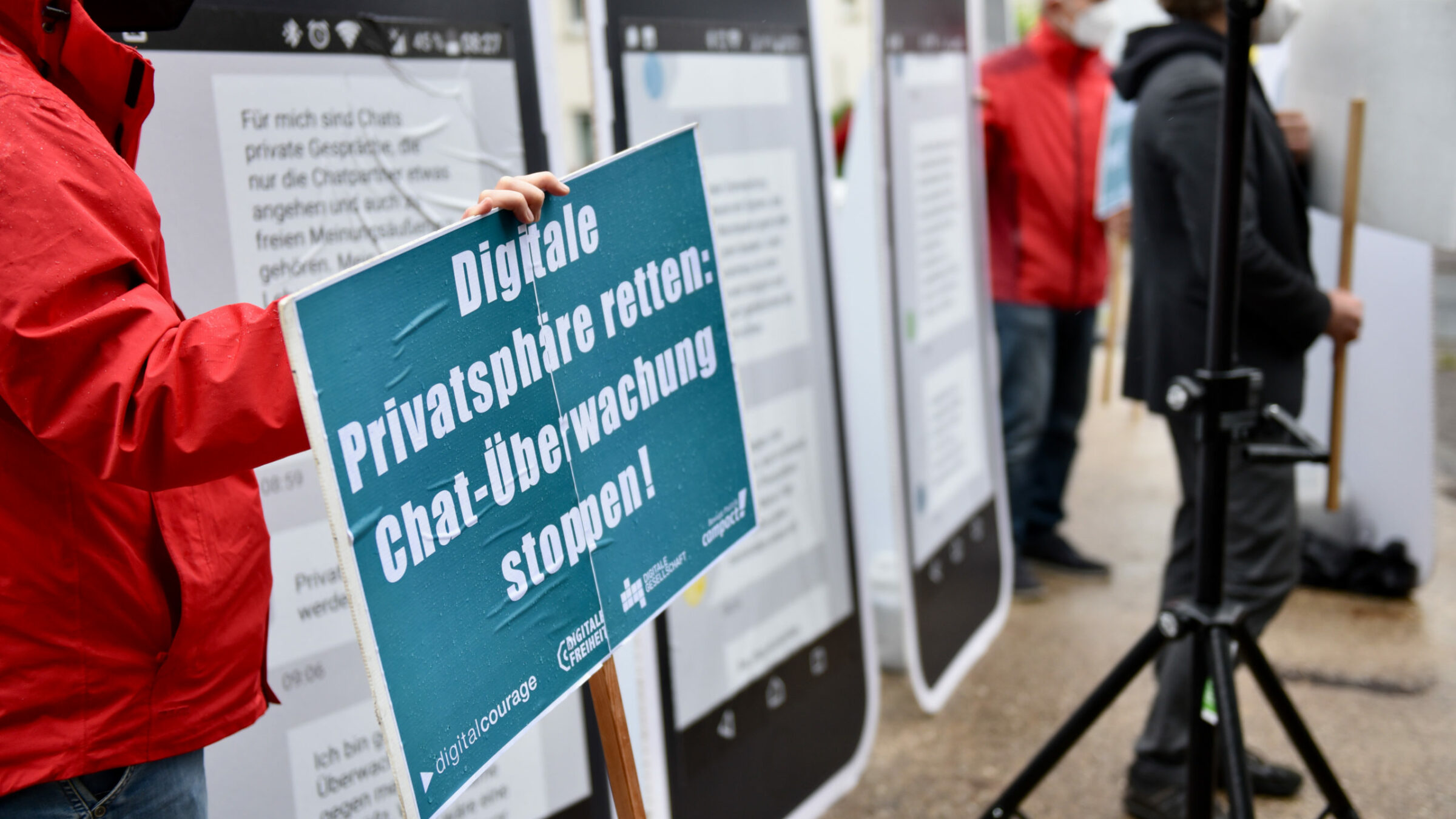 Nahaufnahme einer Person, die ein türkises Schild hält mit der Aufschrift: Digitale Privatsphäre retten: Chat-Überwachung stoppen!"