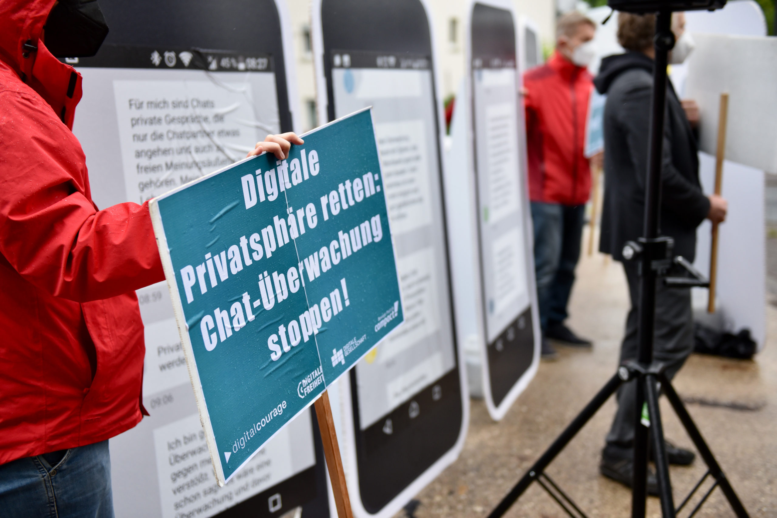 Nahaufnahme einer Person, die ein türkises Schild hält mit der Aufschrift: Digitale Privatsphäre retten: Chat-Überwachung stoppen!"