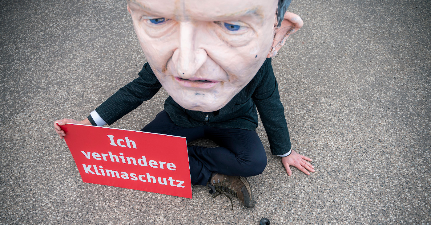 Eine Pappmaché-Figur als Vekehrsminister Wissing hat sich auf die Straße geklebt. In der Hand hält sie ein Schild: Ich verhindere Klimaschutz.