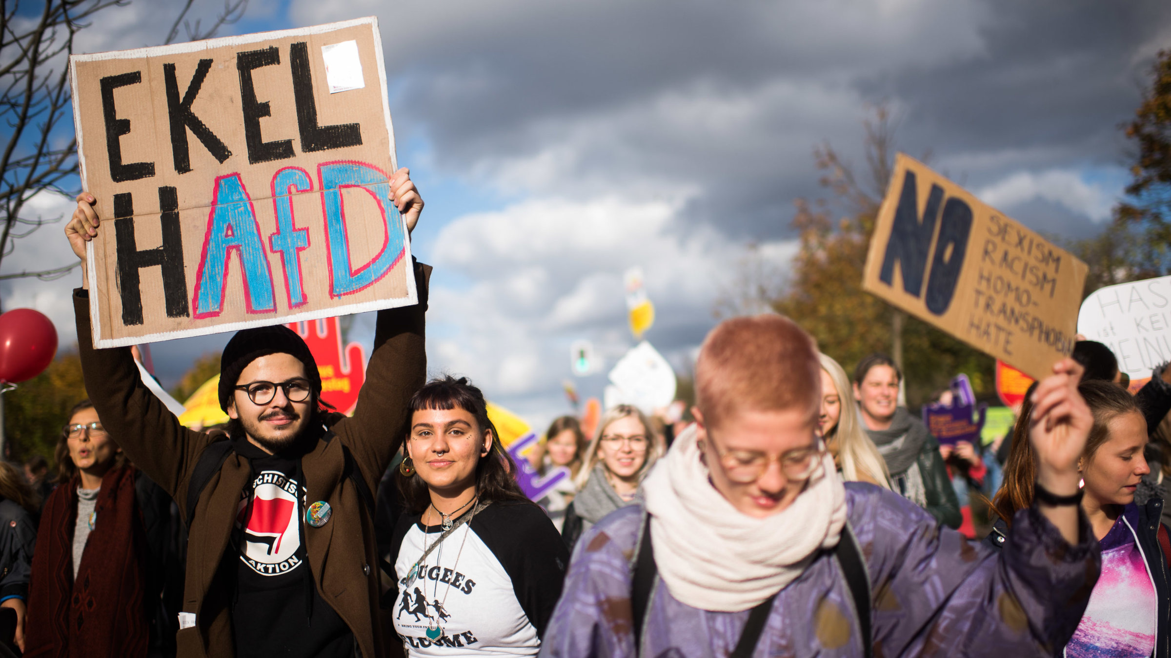 Eine Demo gegen Rechtsextremismus. Zwei Personen halten ein Schild mit der Aufschrift "EkelhAfD" in die Höhe, eine andere Person ein Schild, auf dem steht "No Sexism, Racism, Homo/Transphobia, Hate".