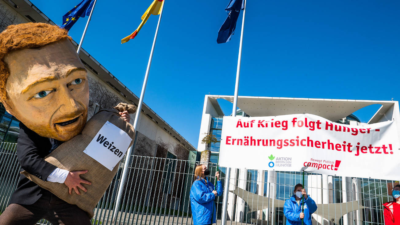 Ein Schauspieler – verkleidet als Finanzminister Lindner mit einer Maske aus Pappmaché – verschüttet wertvolle Lebensmittel. Mit Aktionen wie diesen zur Ernährungssicherheit setzt sich Campact für die Menschenrechte ein.