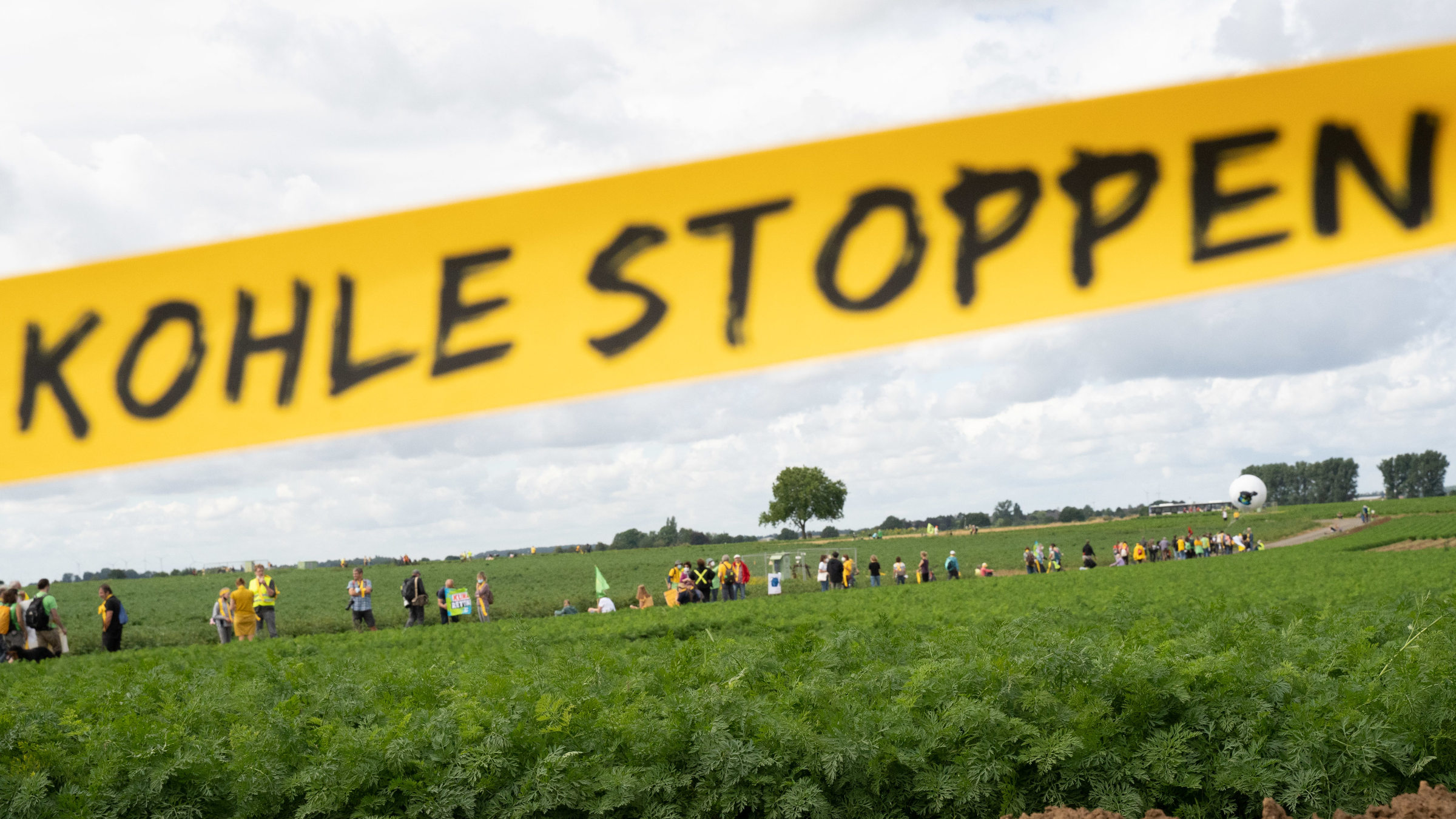 Menschenkette am Tagebau: Auf einem gelben Band ist der Schriftzug "Kohle stoppen" zu lesen.