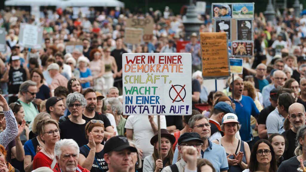 Demokratie-Demos in München. In der Mitte einer Menschenmenge wird ein Schild hochgehalten. Darauf steht: Wer in einer Demokratie schläft, wacht in einer Diktatur auf.