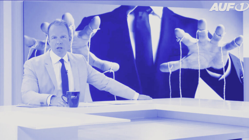 Das Studio von AUF1-TV mit Corona-Betrug: Wer sollte das weltweit inszenieren? AUF1.TV - Stefan Magnet dem Moderator Stefan Magnet am Nachrichtentisch; im Hintergrund ist ein großes Bild mit einer symbolischen Darstellung von Fäden an Händen zu sehen, wie eine Anspielung auf Manipulation oder Steuerung.