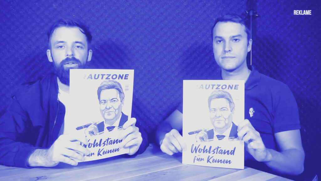 Der rechtsextreme Blogger Miró Wolsfeld und Florian Müller, Gründer des Krautzone Magazin, sitzen an einem Holztisch vor schwarzem Studiovorhang und halten jeweils eine Ausgabe des Magazins Krautzone mit der Titelillustration von Robert Habeck im Stil von Ludwig Erhard mit Zigarre und der Aufschrift „Wohlstand für Keinen“ in die Kamera, oben rechts steht klein Reklame.
